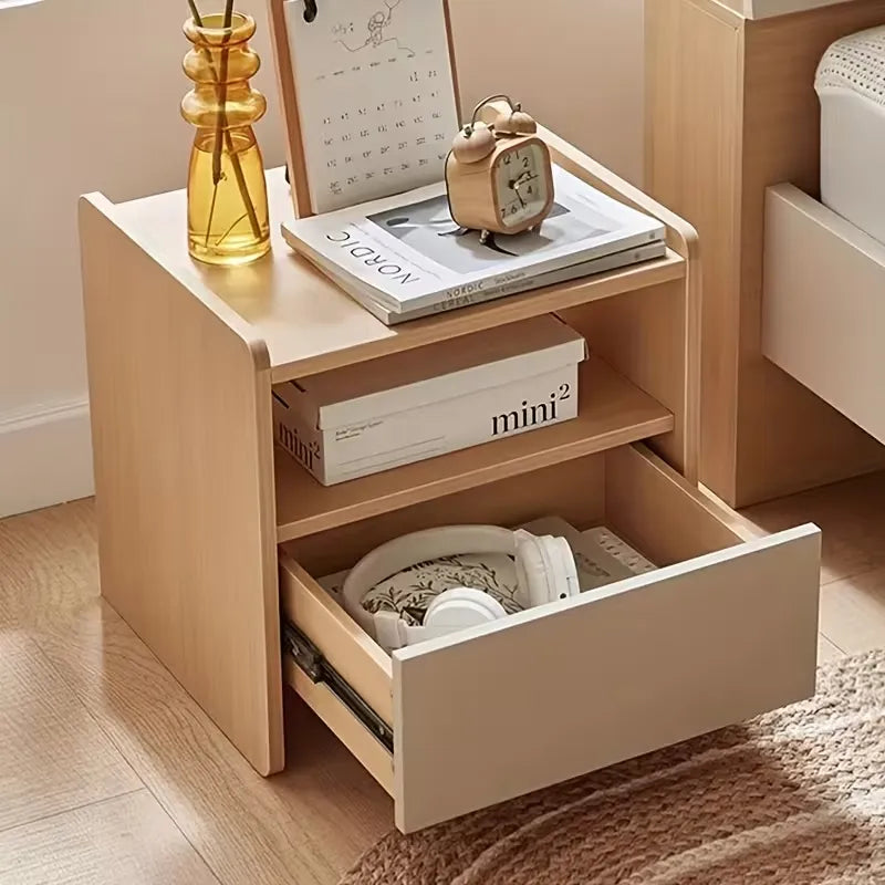 Wooden nightstand with open drawer, books, and decorative items on a wooden floor.