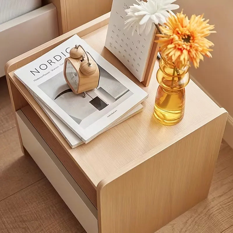 Wooden side table with a magazine, alarm clock, and vase of flowers.