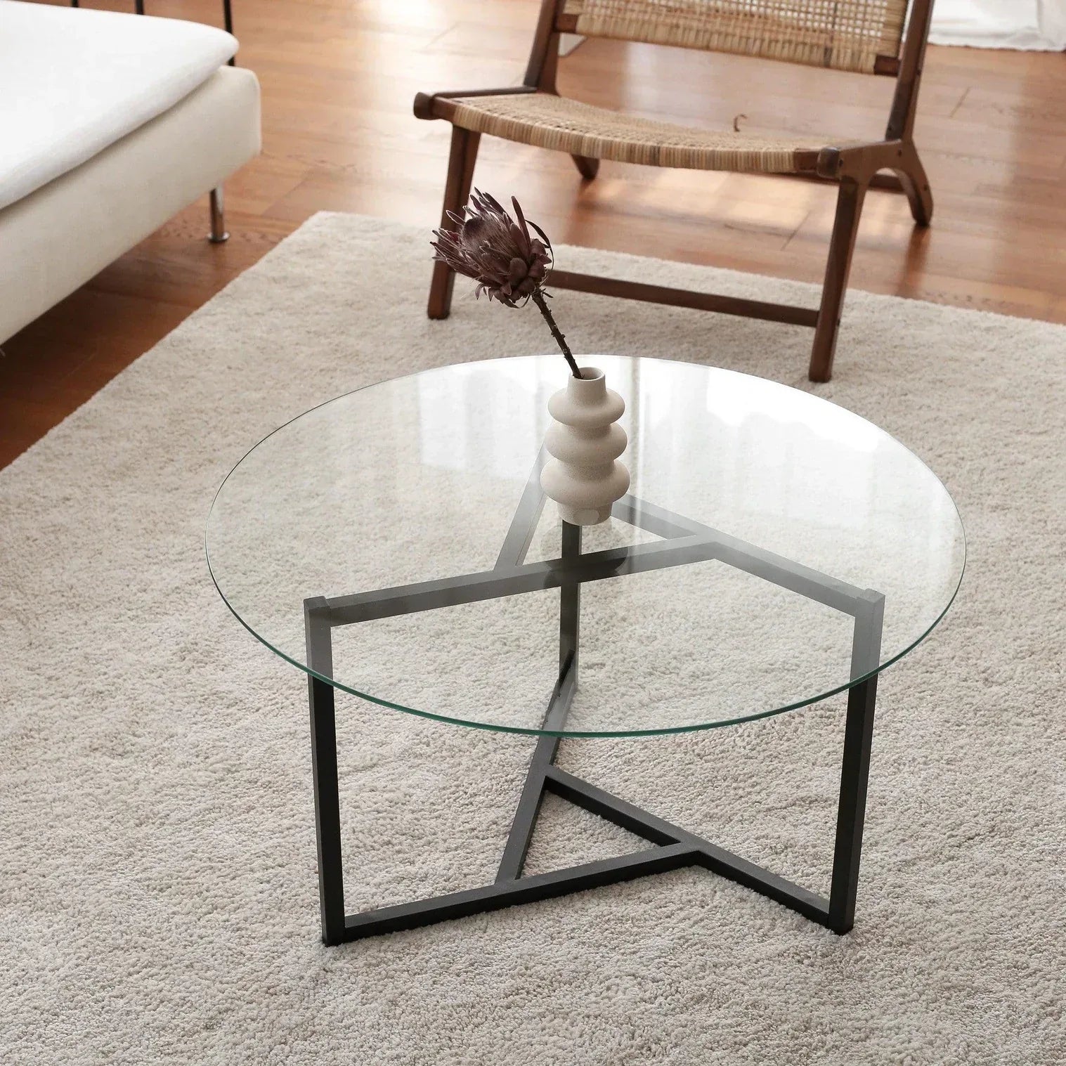 Round glass coffee table with dark metal cross base